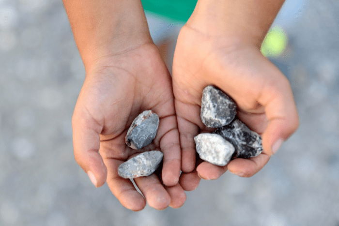Mani di un bambino che esplorano e raccolgono sassi durante un'esperienza con materiali naturali.